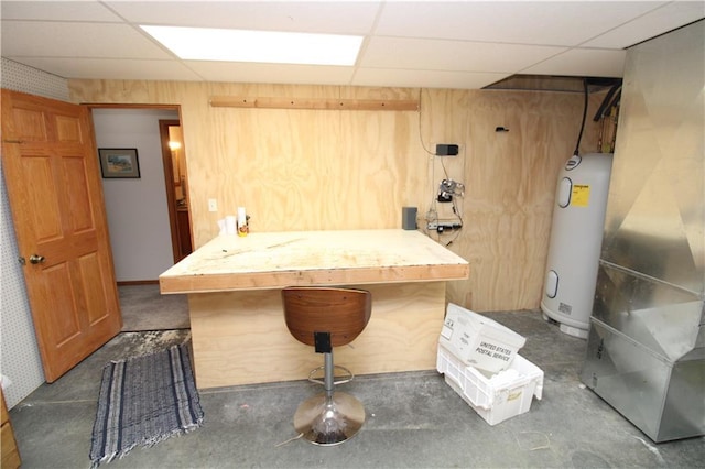 interior space featuring concrete flooring, water heater, wood walls, and a drop ceiling