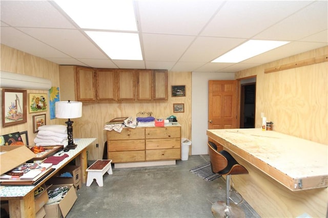 interior space with a paneled ceiling, concrete floors, wood walls, and a workshop area