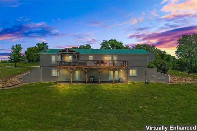 back house at dusk featuring a wooden deck and a lawn