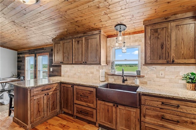 kitchen with kitchen peninsula, sink, hanging light fixtures, light hardwood / wood-style floors, and light stone counters