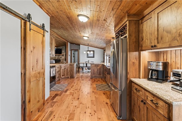 kitchen with stainless steel fridge, light stone counters, wood ceiling, a barn door, and light wood-type flooring