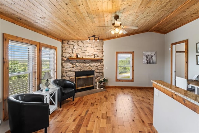 living area with lofted ceiling, wood ceiling, ceiling fan, a stone fireplace, and light wood-type flooring