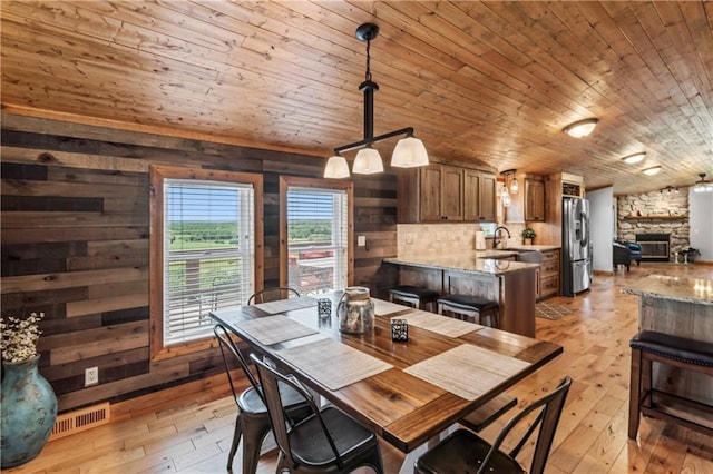 dining space with sink, wood walls, wood ceiling, light hardwood / wood-style flooring, and a fireplace