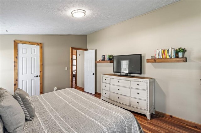 bedroom with dark wood-type flooring, a textured ceiling, and vaulted ceiling