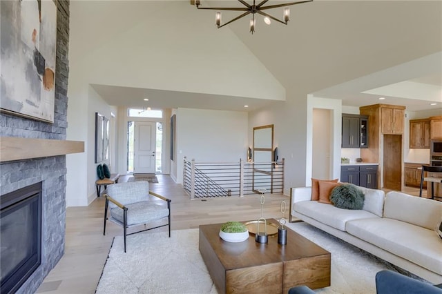 living area with high vaulted ceiling, recessed lighting, light wood finished floors, an inviting chandelier, and a stone fireplace