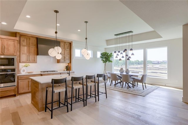 kitchen with pendant lighting, a breakfast bar area, an island with sink, light hardwood / wood-style floors, and stainless steel appliances