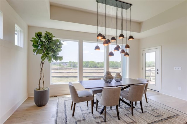 dining space featuring light wood-style floors, visible vents, baseboards, and a raised ceiling
