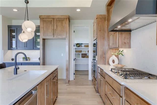 kitchen with glass insert cabinets, a sink, wall chimney range hood, light wood-style floors, and recessed lighting