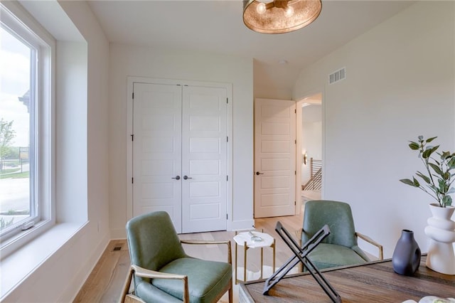 living area featuring light wood finished floors, visible vents, baseboards, and lofted ceiling