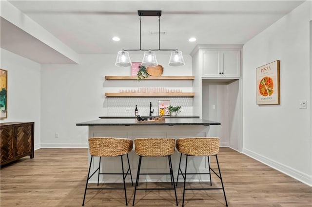 kitchen with white cabinets, light hardwood / wood-style flooring, a kitchen island with sink, and a breakfast bar area