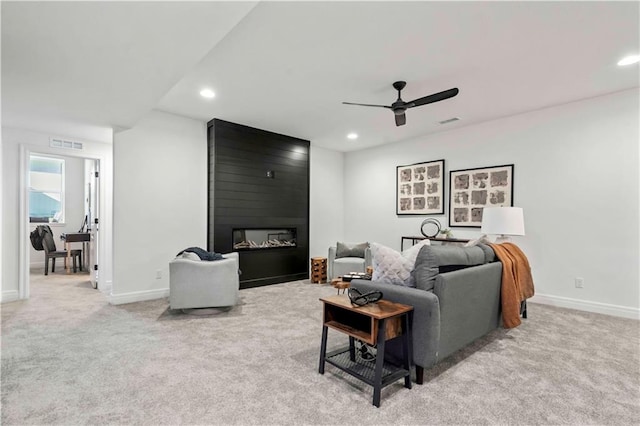 living room featuring ceiling fan, a large fireplace, and light carpet