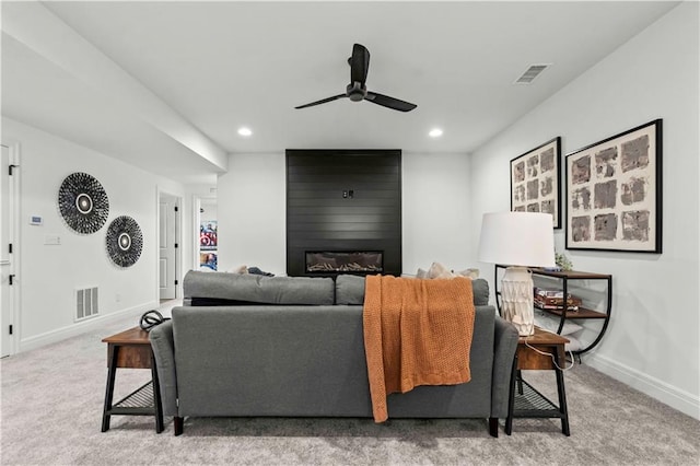 living room featuring a large fireplace, ceiling fan, and carpet