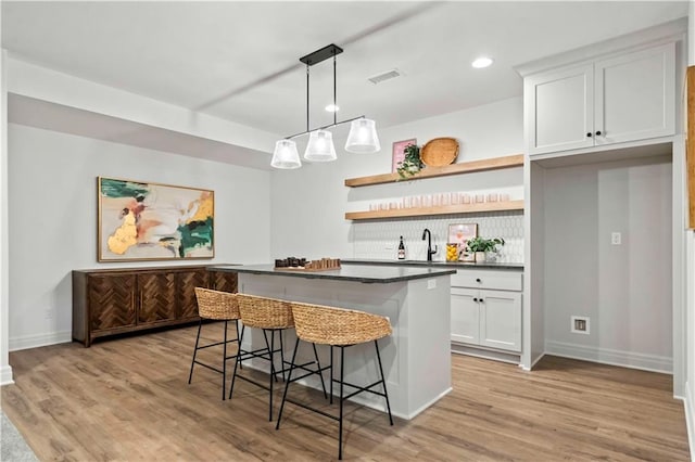 kitchen with white cabinets, light wood-type flooring, a breakfast bar area, and pendant lighting