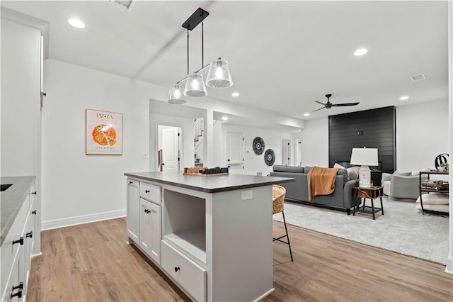 kitchen featuring white cabinets, a kitchen island, decorative light fixtures, light hardwood / wood-style floors, and a kitchen breakfast bar