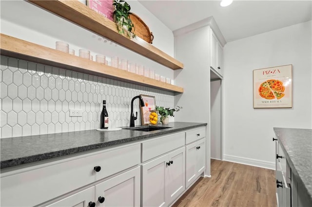 kitchen with decorative backsplash, sink, white cabinetry, and light hardwood / wood-style flooring