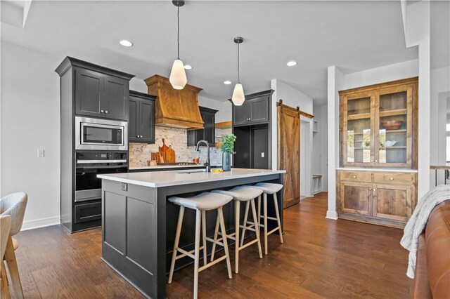 kitchen featuring appliances with stainless steel finishes, tasteful backsplash, hanging light fixtures, a barn door, and a center island with sink