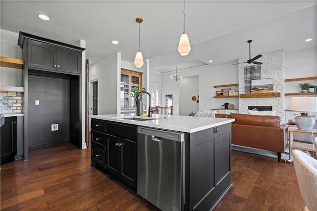 kitchen featuring a stone fireplace, dishwasher, a kitchen island with sink, sink, and pendant lighting