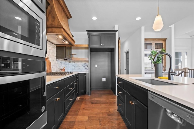 kitchen featuring pendant lighting, appliances with stainless steel finishes, sink, backsplash, and premium range hood