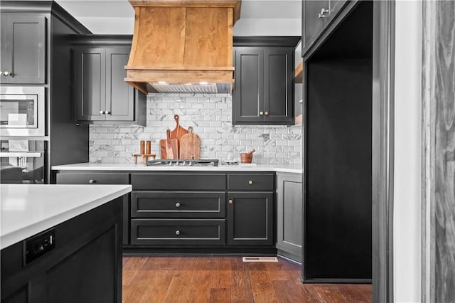 1600 SW 27th St, Lees Summit, MO 64082 - kitchen with custom exhaust hood, light countertops, decorative backsplash, appliances with stainless steel finishes, and dark wood-type flooring