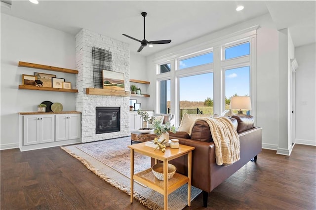 living room featuring ceiling fan, a stone fireplace, and dark hardwood / wood-style flooring