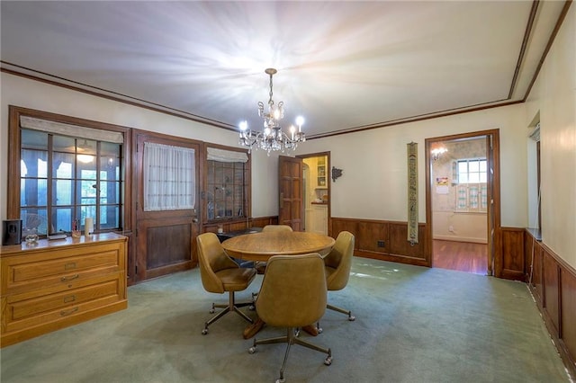 dining room featuring wooden walls, light carpet, ornamental molding, and an inviting chandelier