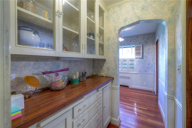 kitchen with light wood-type flooring, ornamental molding, butcher block countertops, white cabinetry, and radiator heating unit