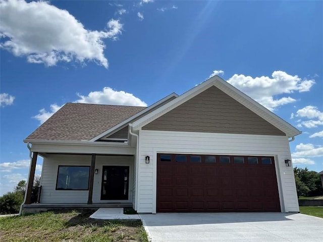 view of front of home featuring an attached garage, driveway, a shingled roof, and covered porch