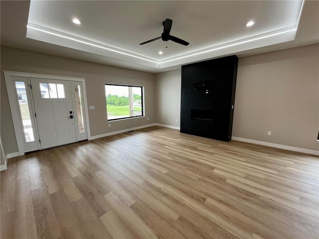 entrance foyer featuring a fireplace, a raised ceiling, light wood-style flooring, and baseboards