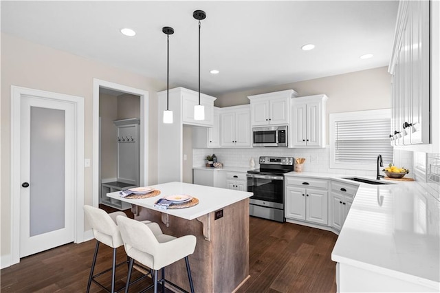 kitchen with appliances with stainless steel finishes, dark hardwood / wood-style floors, white cabinetry, decorative backsplash, and hanging light fixtures