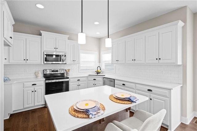 kitchen with a kitchen island, white cabinetry, appliances with stainless steel finishes, and decorative light fixtures