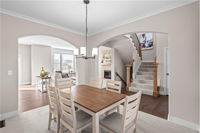 dining space featuring an inviting chandelier, dark hardwood / wood-style flooring, crown molding, and a stone fireplace