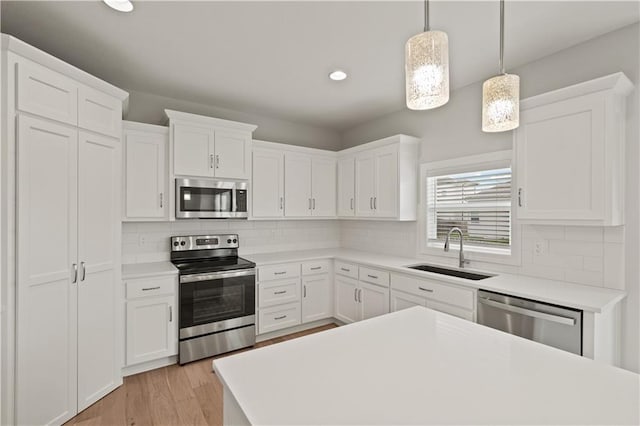 kitchen with sink, white cabinetry, stainless steel appliances, and hanging light fixtures