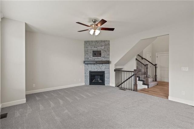 unfurnished living room featuring ceiling fan, a stone fireplace, and light carpet