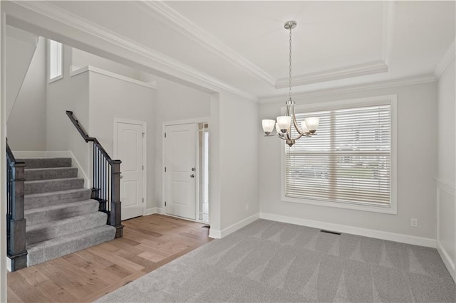 entrance foyer with a raised ceiling, an inviting chandelier, light hardwood / wood-style flooring, and crown molding