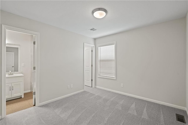 unfurnished bedroom featuring light carpet, connected bathroom, and sink