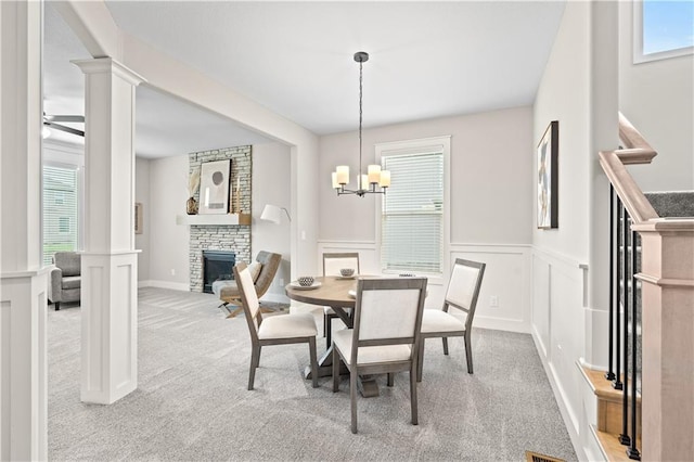 dining room with a fireplace, plenty of natural light, light colored carpet, and ceiling fan with notable chandelier