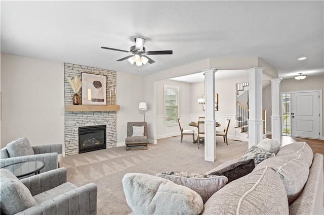 carpeted living room with a fireplace, ornate columns, and ceiling fan