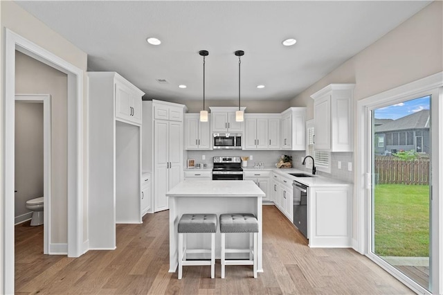 kitchen with appliances with stainless steel finishes, white cabinetry, a kitchen island, and light hardwood / wood-style floors