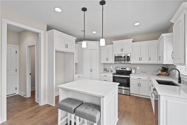 kitchen with appliances with stainless steel finishes, sink, light hardwood / wood-style flooring, white cabinets, and a center island