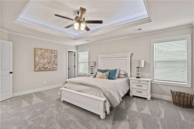 carpeted bedroom featuring ceiling fan, ornamental molding, a tray ceiling, and multiple windows