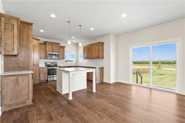 kitchen with hanging light fixtures, dark hardwood / wood-style floors, appliances with stainless steel finishes, tasteful backsplash, and a kitchen island