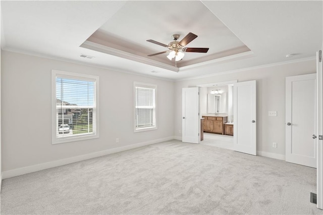 unfurnished bedroom featuring ceiling fan, light colored carpet, connected bathroom, and a tray ceiling