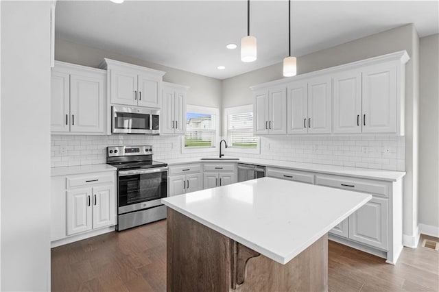 kitchen with dark wood-type flooring, stainless steel appliances, a center island, and white cabinets