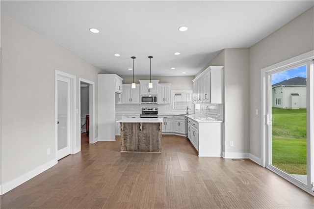 kitchen featuring decorative light fixtures, dark hardwood / wood-style flooring, a kitchen island, stainless steel appliances, and white cabinets