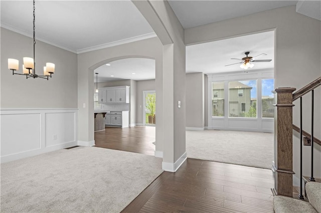 entryway with crown molding, ceiling fan with notable chandelier, a wealth of natural light, and dark carpet