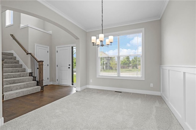 foyer with ornamental molding, a chandelier, and dark carpet