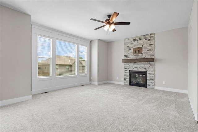 unfurnished living room with light carpet, a stone fireplace, and ceiling fan