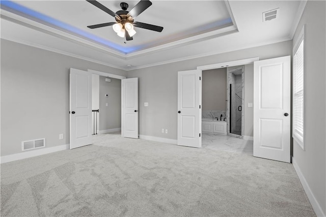 unfurnished bedroom with connected bathroom, light carpet, ornamental molding, a raised ceiling, and ceiling fan