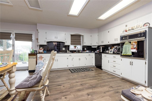 kitchen featuring a textured ceiling, white cabinets, black appliances, tasteful backsplash, and light hardwood / wood-style flooring