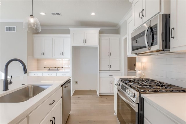 kitchen with white cabinetry, sink, hanging light fixtures, ornamental molding, and stainless steel appliances